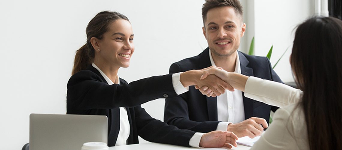 Smiling HR managers greeting female job applicant with handshake during recruiting or interview. Businesswoman making good first impression shaking hands of business partners. Partnership, cooperation